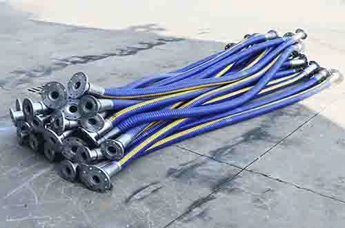 Industrial composite hoses with flanged ends stacked outdoors.