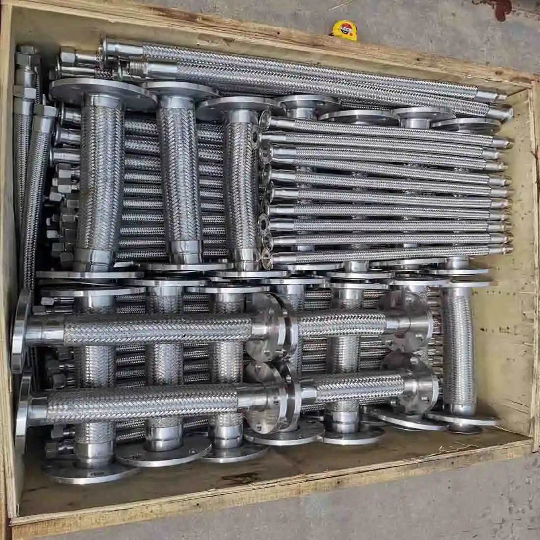Metal hoses with flanged ends stacked in a wooden crate.